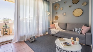 Ein modernes Wohnzimmer mit einem grauen Sofa, einem runden Couchtisch und einem Balkon mit Blumentöpfen.