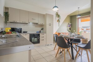 A modern kitchen with a dining area, featuring a kitchen island, built-in appliances, and a dining table set for four. - Hygge Family Apartment (Sirmione)