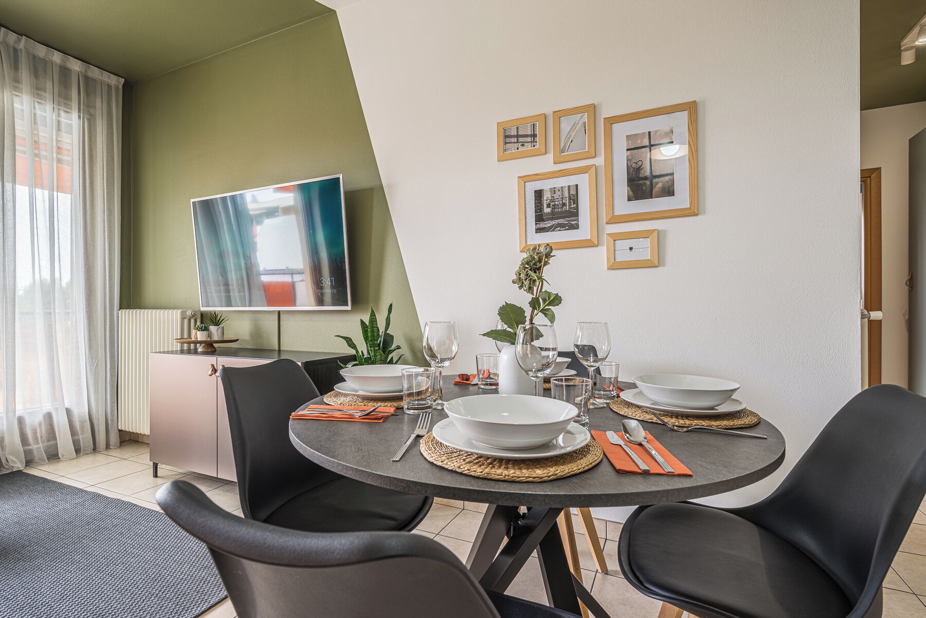 Un coin repas avec une table ronde, des chaises noires et un téléviseur à écran plat fixé au mur.