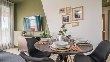 Un coin repas avec une table ronde, des chaises noires et un téléviseur à écran plat fixé au mur.
