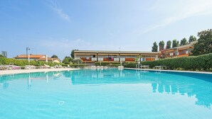 A swimming pool with lounge chairs, a building with balconies, and a clear sky. - Luminoso Appartamento con piscina secondo piano (Sirmione)