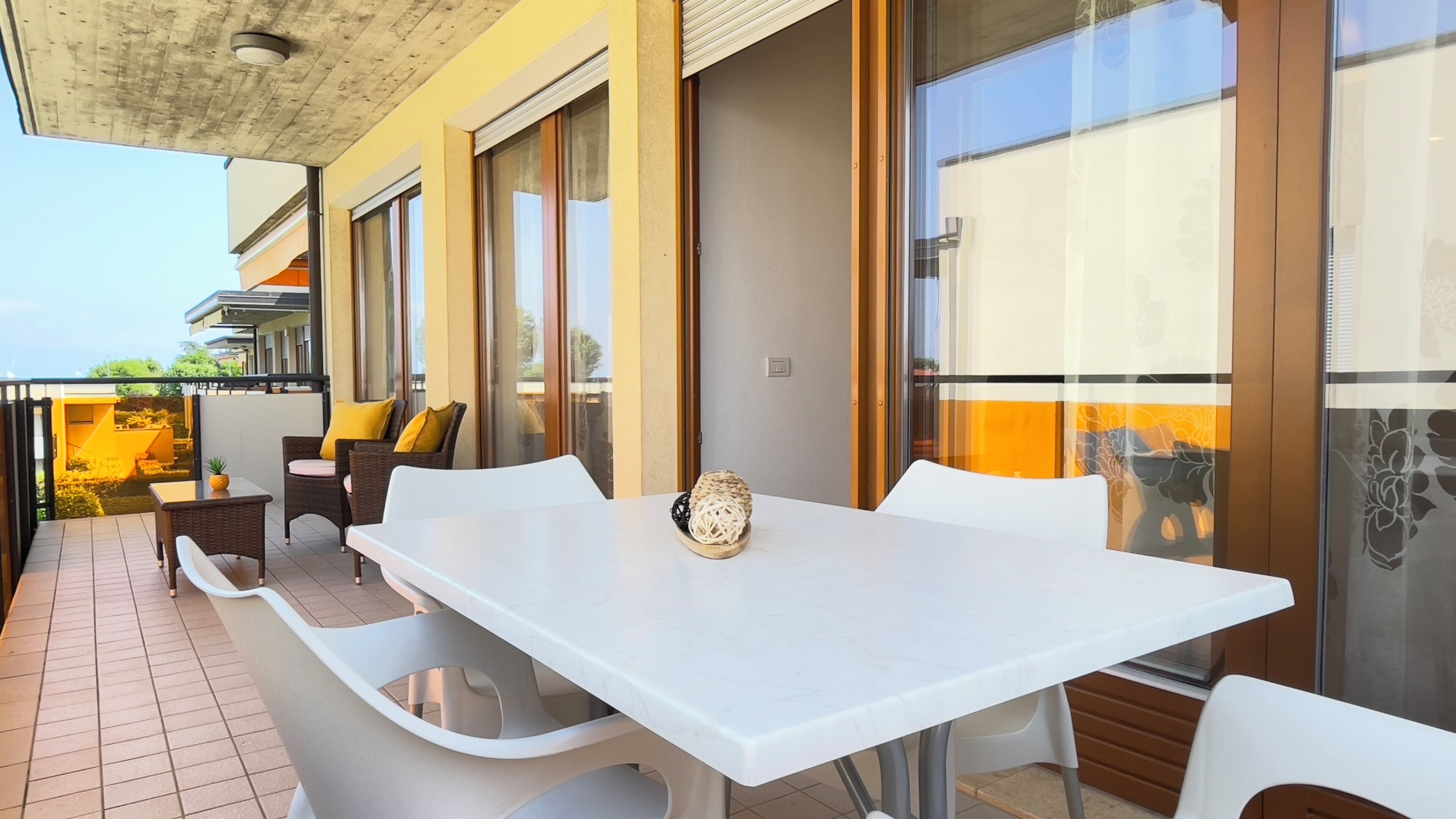 Una terraza con una mesa blanca, sillas de mimbre y un ventanal que da a un balcón.