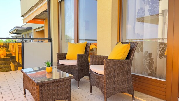 A balcony with wicker furniture, a glass table, and a potted plant. - Luminoso Appartamento con piscina secondo piano (Sirmione)