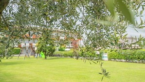 An outdoor area with a lawn, trees, and a building in the background. - Luminoso Appartamento con piscina secondo piano (Sirmione)