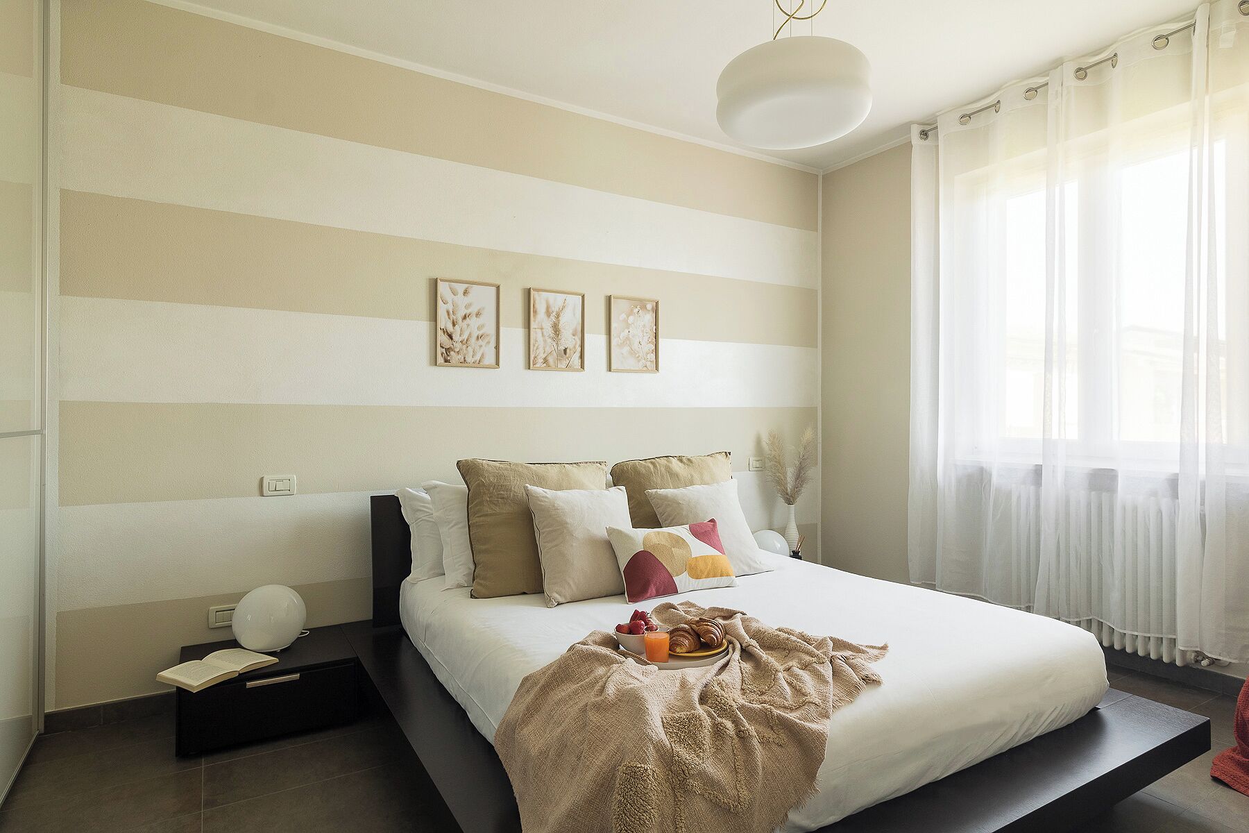 Un dormitorio con cama, mesitas de noche, lámparas de noche y una ventana con cortinas translúcidas.
