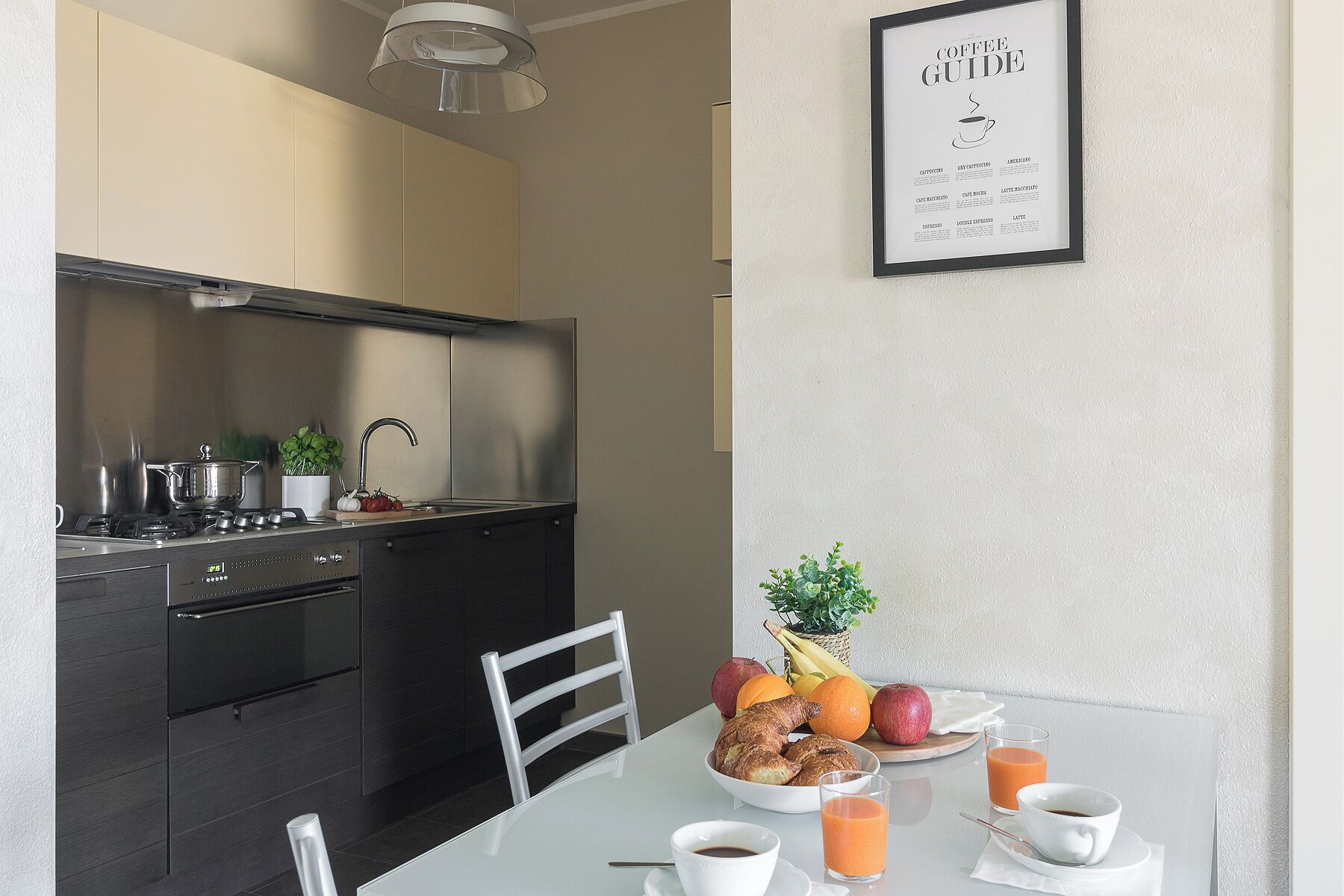 Una cocina moderna con una mesa de desayuno dispuesta, que incluye cruasanes, fruta y café.