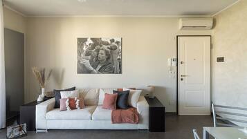 Una sala de estar con un sofá, una fotografía enmarcadas en la pared, un equipo de aire acondicionado y una puerta.