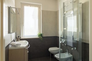 Ein modernes Badezimmer mit Duschkabine aus Glas, Toilette, Waschbecken und Spiegel.