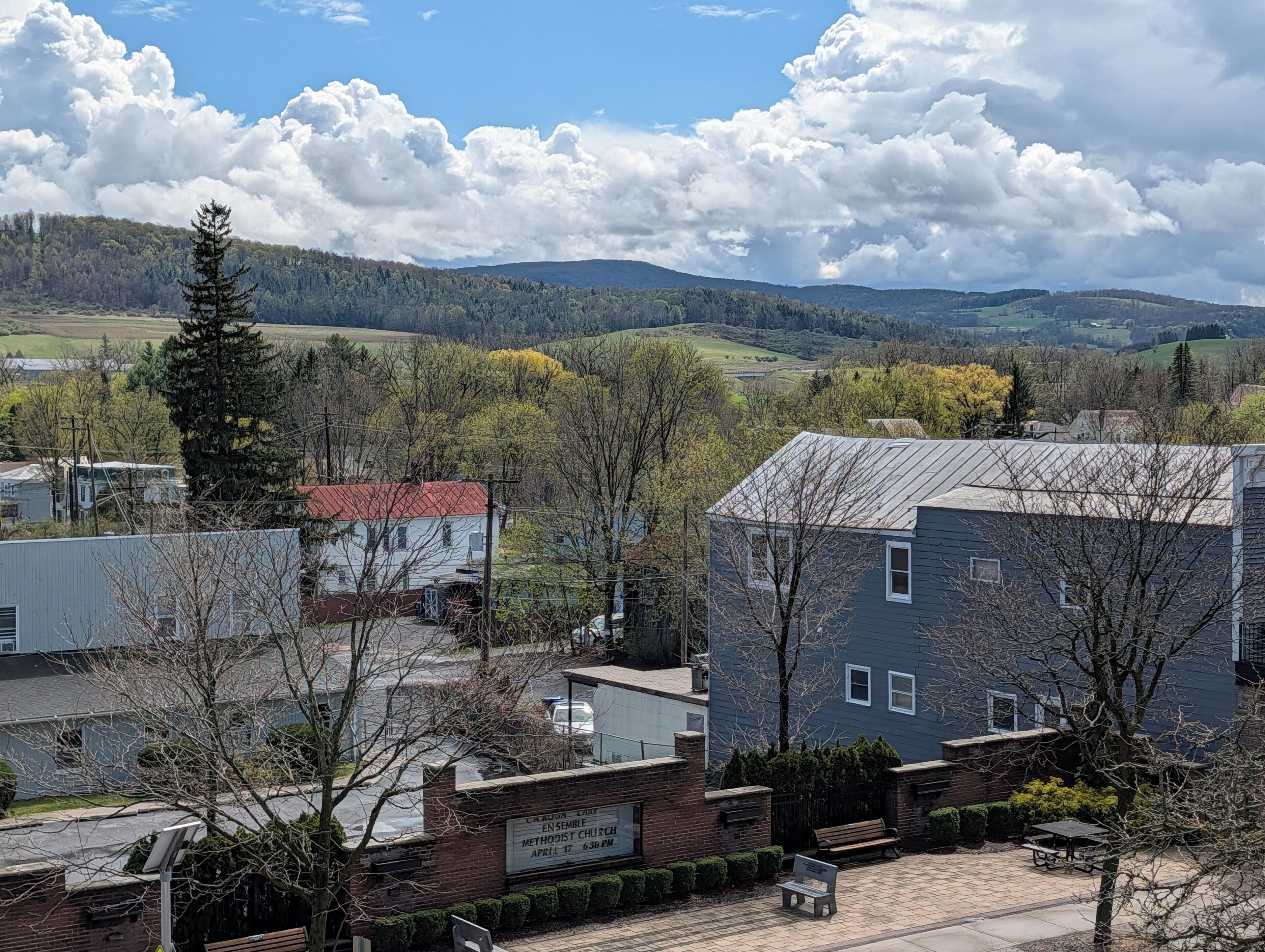 A building with a sign indicating a Methodist Church, surrounded by trees and a view of hills.
