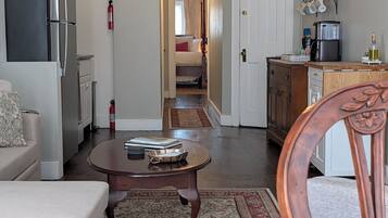 Cocina moderna con refrigerador, estufa y cafetera. Cuenta con una zona de comedor con mesa y sillas, y un pasillo que conduce a un dormitorio.