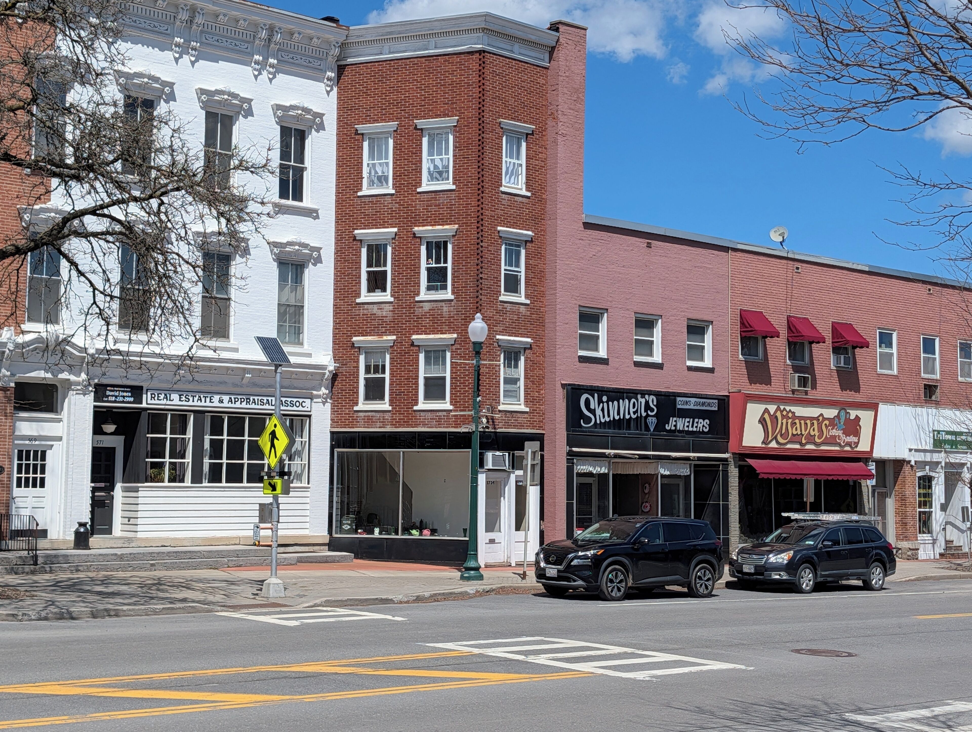 A street view with buildings, including a real estate office, a jewelry store, and a fashion boutique.