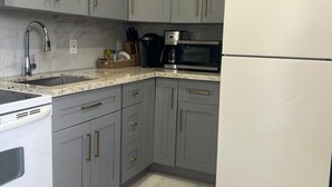 Une cuisine avec des meubles gris, un réfrigérateur blanc, un four à micro-ondes, une machine à café et une cuisinière.