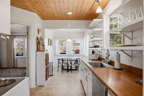 Une cuisine moderne avec des meubles blancs, un plafond en bois et un coin repas comprenant une table et des chaises.