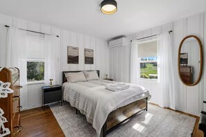Une chambre à coucher comprenant un lit, une table de chevet, une commode, une fenêtre avec des rideaux et un miroir.