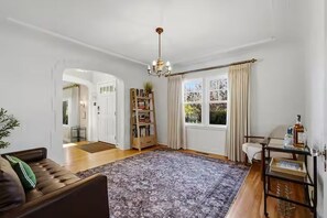 Ein geräumiges Wohnzimmer mit großem Teppich, einer braunen Ledersofa, einem Bücherregal und einem Fenster mit Vorhängen.