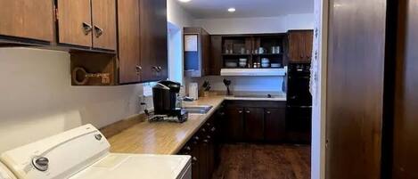 A compact kitchen with wooden cabinets, a white washing machine, and a black refrigerator.