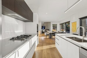 Eine moderne Küche mit einer zentralen Kochinsel, einem Essbereich mit Tisch und Stühlen und Blick ins Freie durch große Fenster.