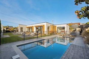 Ein modernes Haus mit Swimmingpool, umzäunter Garten und blauem Himmel.