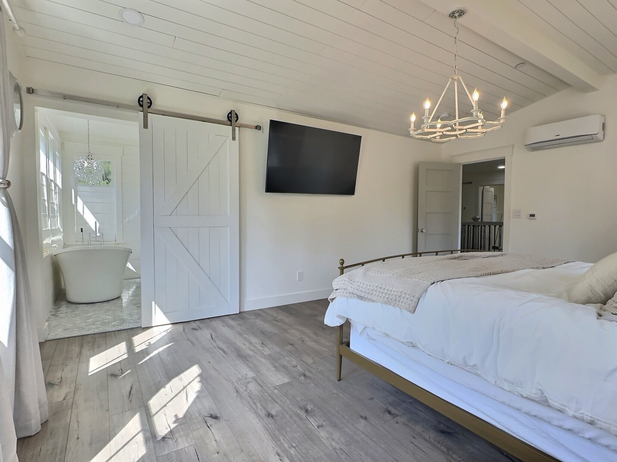 Un dormitorio con cama, candelabro, puerta corredera y televisor en la pared.