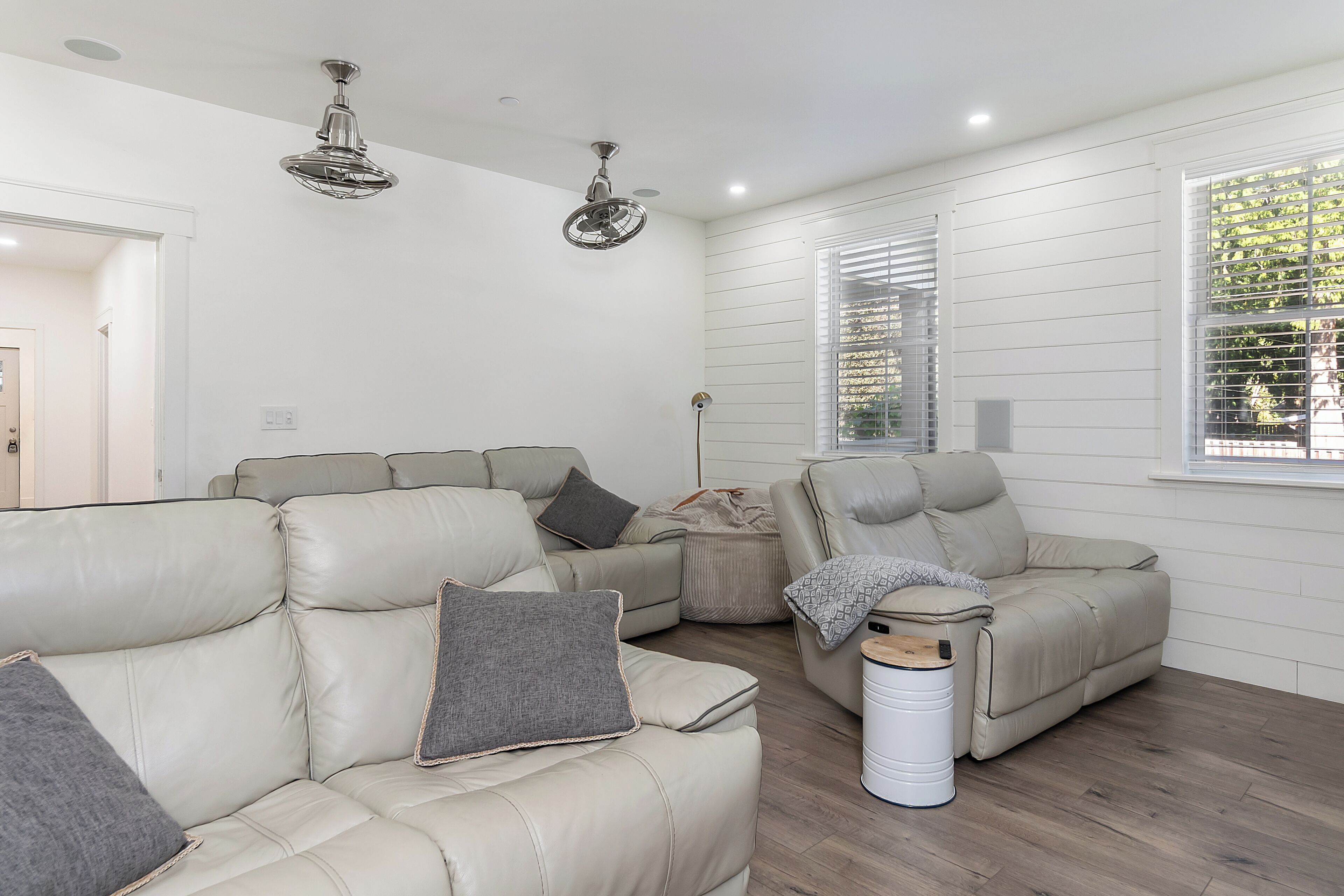 A modern living room with two beige leather sofas, a white trash bin, and a ceiling fan.