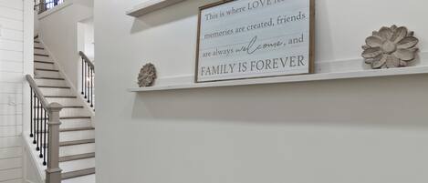 Een trap met een leuning en een muur met een lijst waarop staat: 'Hier woont de LIEFDE, herinneringen worden geschapen, vrienden zijn altijd welkom en FAMILIE IS EEUWIG'.