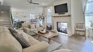A modern living room with a fireplace, a television, and a staircase leading to a kitchen. - Serene 5BR Farmhouse Retreat Shoreline (Shoreline)
