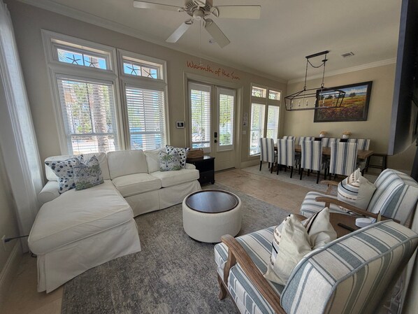 A living room with a sectional sofa, a round ottoman, a dining area with striped chairs, and a ceiling fan. - Endless Summer House , Lagoon Pool, Private Beach, Bikes (Inlet Beach)