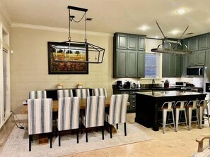 A modern kitchen with green cabinets, a dining area with striped chairs, and a hanging light fixture. - Endless Summer House , Lagoon Pool, Private Beach, Bikes (Inlet Beach)