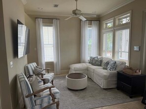 A living room with a sectional sofa, two armchairs, a round ottoman, a ceiling fan, and a TV mounted on the wall. - Endless Summer House , Lagoon Pool, Private Beach, Bikes (Inlet Beach)