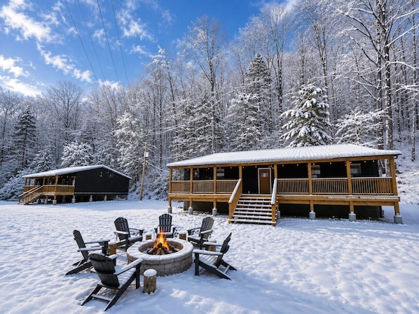 Una cabaña con terraza, fogón y árboles cubiertos de nieve.
