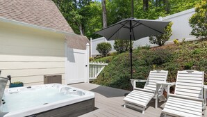 Eine Terrasse mit Whirlpool, weißen Liegestühlen und Sonnenschirm.