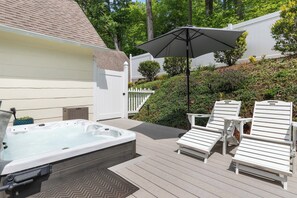 Une terrasse avec un jacuzzi, des chaises longues blanches et un parasol.