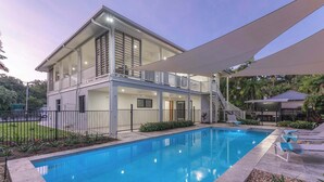 Una casa de dos pisos con piscina, un patio cubierto y un balcón.