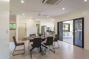 A modern kitchen with white cabinets, a dining area with a table and chairs, and a sliding glass door leading to an outdoor area. - Papaya Beach House - Port Douglas (Port Douglas)