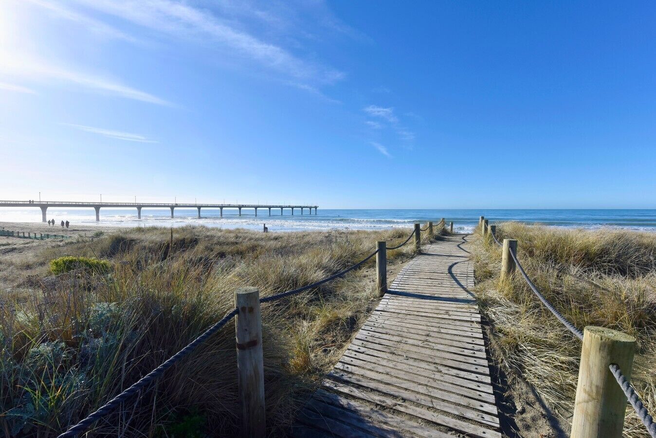 Une promenade en bois qui mène à une plage, avec une jetée en arrière-plan.