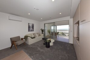 A modern living room with a sofa, a coffee table, and a balcony with a view. - Beachfront Stay with Balcony & Ocean Views (Christchurch)