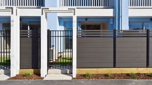 A gated entrance to a building with numbered gates, a paved pathway, and a small garden area. - Coastal 1BR Retreat – Steps to New Brighton Beach (Christchurch)