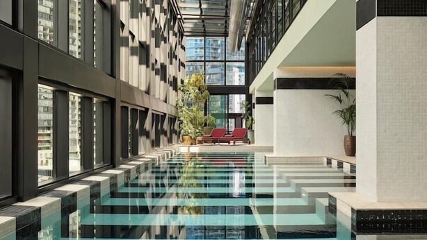 A modern indoor pool with glass walls, a clear ceiling, and a view of the cityscape. - Southbank Level 51 Panoramic Views w/ Pool & Sauna (Southbank)