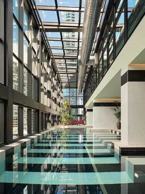 En modern inomhuspool med glasväggar, ett genomskinligt tak och utsikt över stadsbilden.