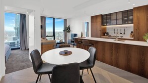 A modern apartment with a dining area, kitchen, and a large window with a city view. - Southbank Level 51 Panoramic Views w/ Pool & Sauna (Southbank)