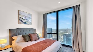 A modern hotel room with a large bed, a nightstand, a lamp, and a city view through large windows. - Southbank Level 51 Panoramic Views w/ Pool & Sauna (Southbank)