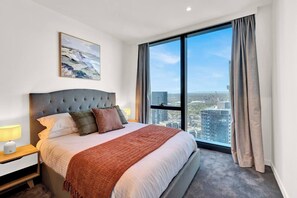 Une chambre d’hôtel moderne avec un grand lit, une table de chevet, une lampe et une vue sur la ville grâce à de grandes fenêtres.