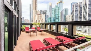 A rooftop terrace with red lounge chairs, a wooden deck, and a city skyline view. - Southbank Level 51 Panoramic Views w/ Pool & Sauna (Southbank)