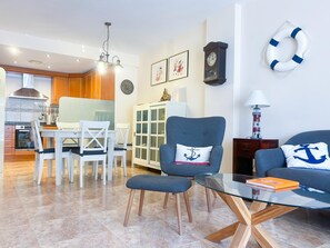 Un salon moderne avec une table basse en verre, un fauteuil bleu et un canapé agrémenté de coussins aux motifs marins.