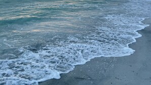 Una playa con olas, cielo nublado y un atardecer.