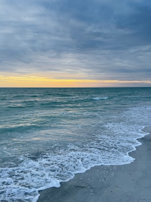 Ein Strand mit Wellen, bewölktem Himmel und Sonnenuntergang.