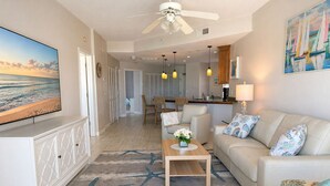 A living room with a TV, a sofa, a coffee table, and a dining area with chairs. - Upscale Beachfront Condo • Gulf View Balcony • Pool• Steps to Johns Pass &Dining (Madeira Beach)