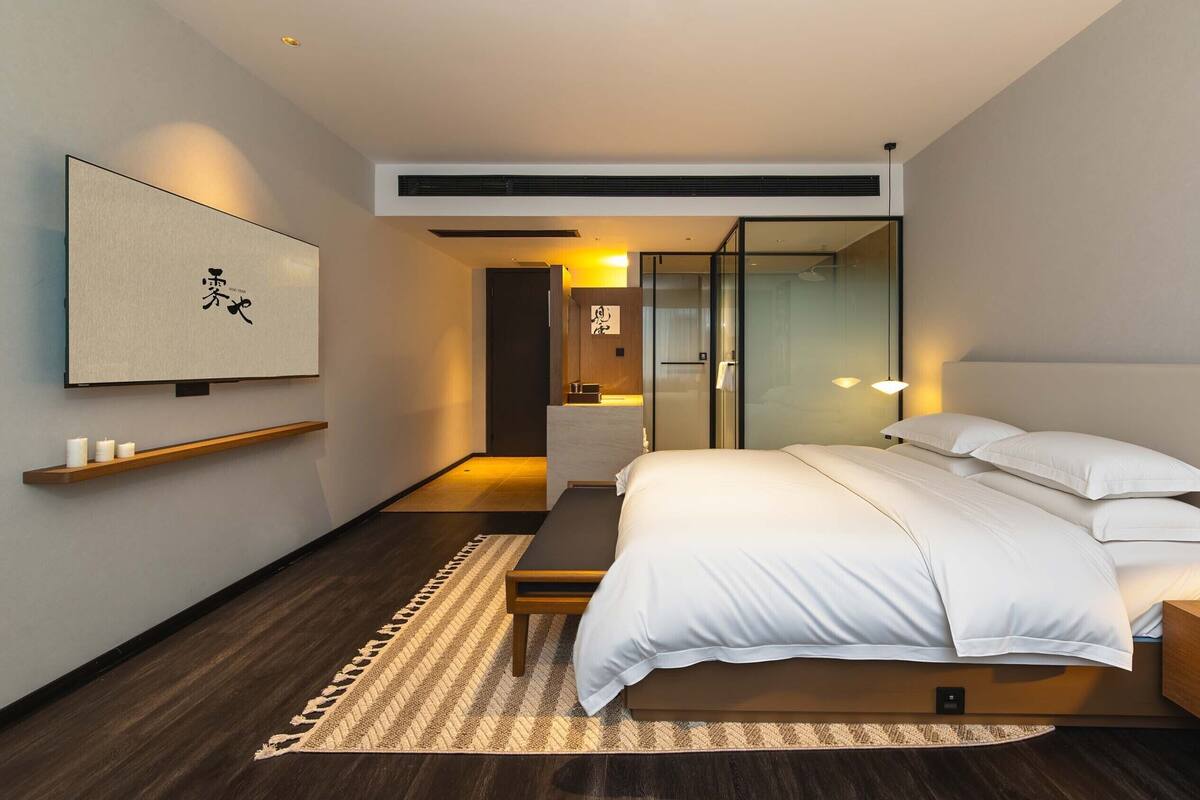 A modern hotel room with a bed, bedside table, bedside lamp, and a wall-mounted artwork.