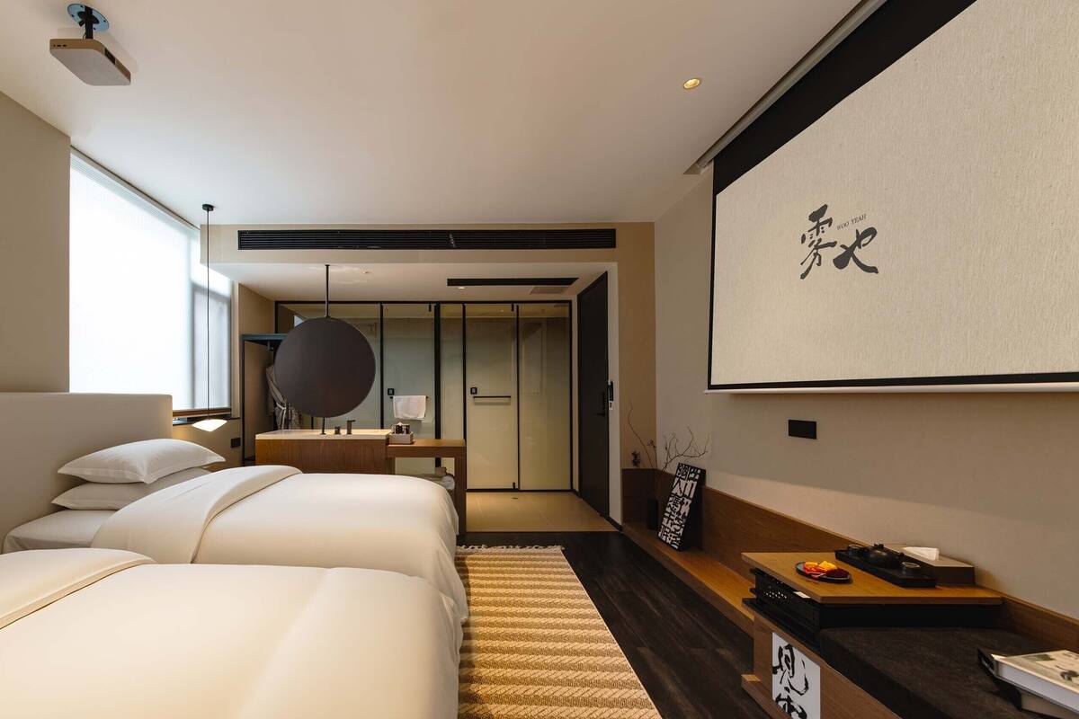 A modern hotel room with a large bed, a desk, and a view of the hallway.