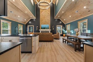 Una cocina amplia con una isla central, un comedor con mesa y bancos de madera, y una sala de estar con chimenea.